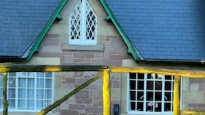 Een vakantiehuisje met een stenen gevel, een groen dak en een houten poortje met de tekst 'Rose Cottage'.