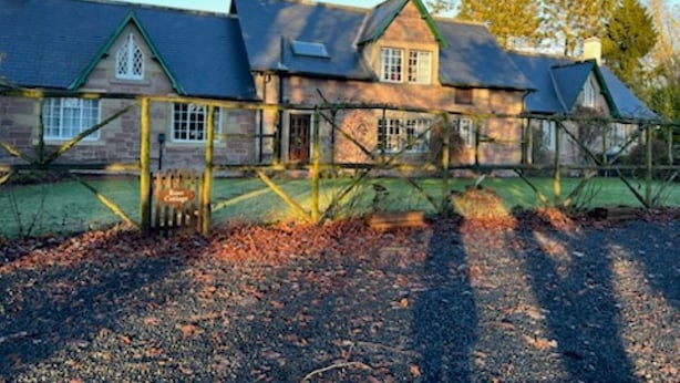 Een groot, klassiek stenen huis met meerdere schoorstenen, een hekpoort en een keurig onderhouden tuin met een grindpad.
