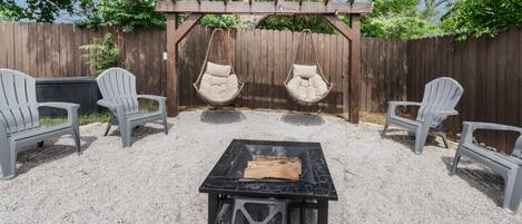 A backyard patio with a black metal table, two Adirondack chairs, and two hanging chairs.