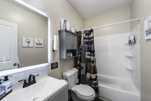 Ein Badezimmer mit einem weißen Waschbecken, einer Toilette und einer Badewanne. An der Wand hängen zwei gerahmte Bilder, ein Handtuchhalter und ein Schild über der Toilette.