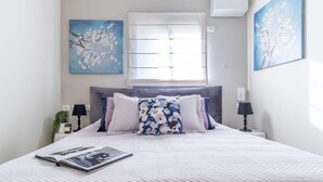 A neatly made bed with a magazine, two wall-mounted lamps, and a window with blinds. - Fantastic 1BR Apartment with Parking in the city center (Jerusalem)