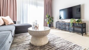 A modern living room with a grey sofa, a round coffee table, a TV, and a plant. - Fantastic 1BR Apartment with Parking in the city center (Jerusalem)