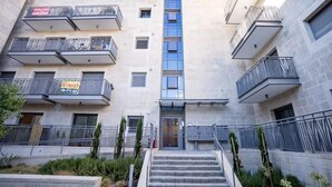 A multi-story building with balconies, a central entrance, and a staircase leading to the entrance. - Fantastic 1BR Apartment with Parking in the city center (Jerusalem)