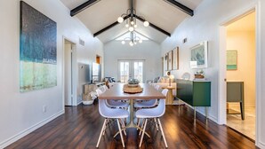 Un vaste espace dédié  à la salle à manger, avec une longue table en bois, des chaises blanches et un lustre moderne.