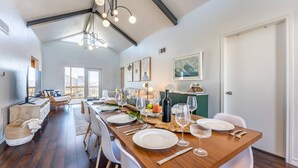 Un espace repas avec une longue table en bois dressée pour un repas, entourée de chaises blanches.