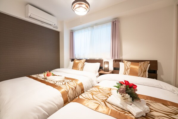 Habitación de hotel con dos camas, una ventana con cortinas, un equipo de aire acondicionado y una mesita de noche con lámpara.