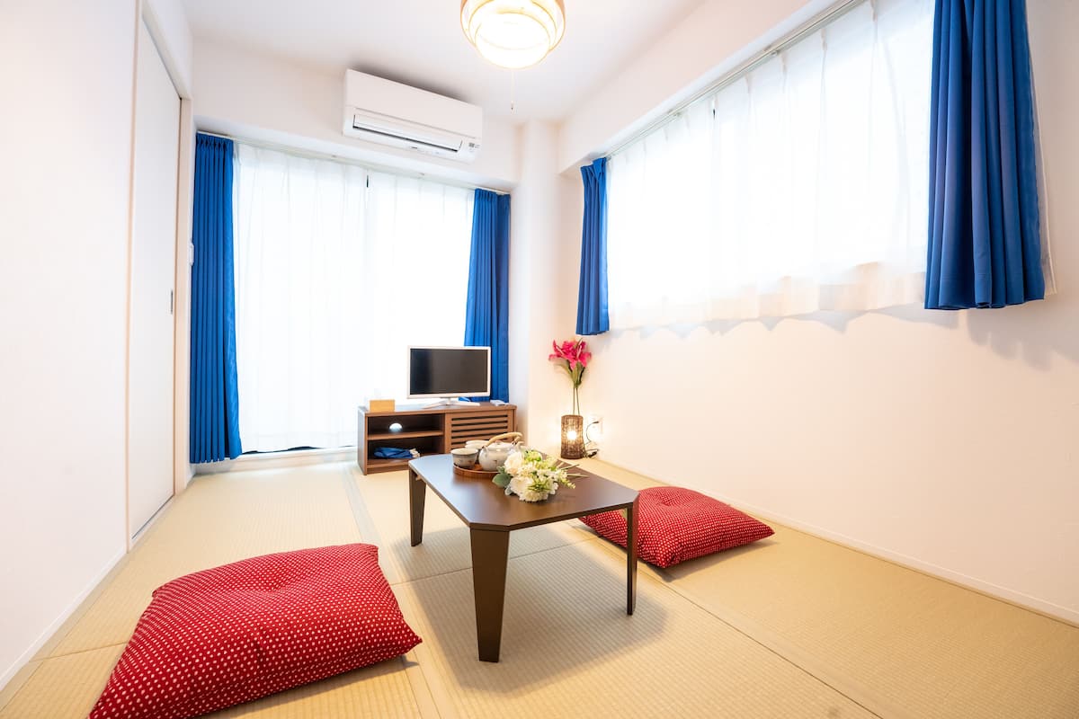 Quarto com piso de tatame, televisão, mesa com vaso e flores, e almofadas vermelhas.
