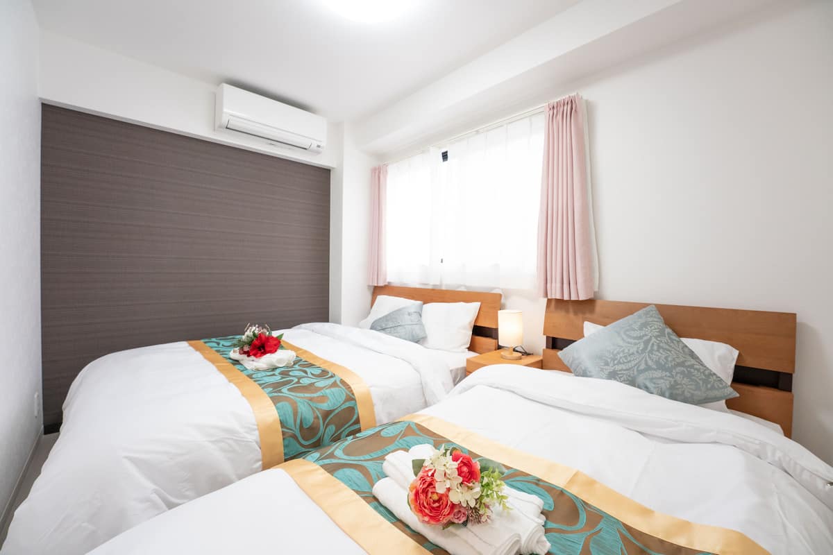 Quarto de hotel com duas camas, janela com cortinas, ar condicionado e mesa de cabeceira com abajur.