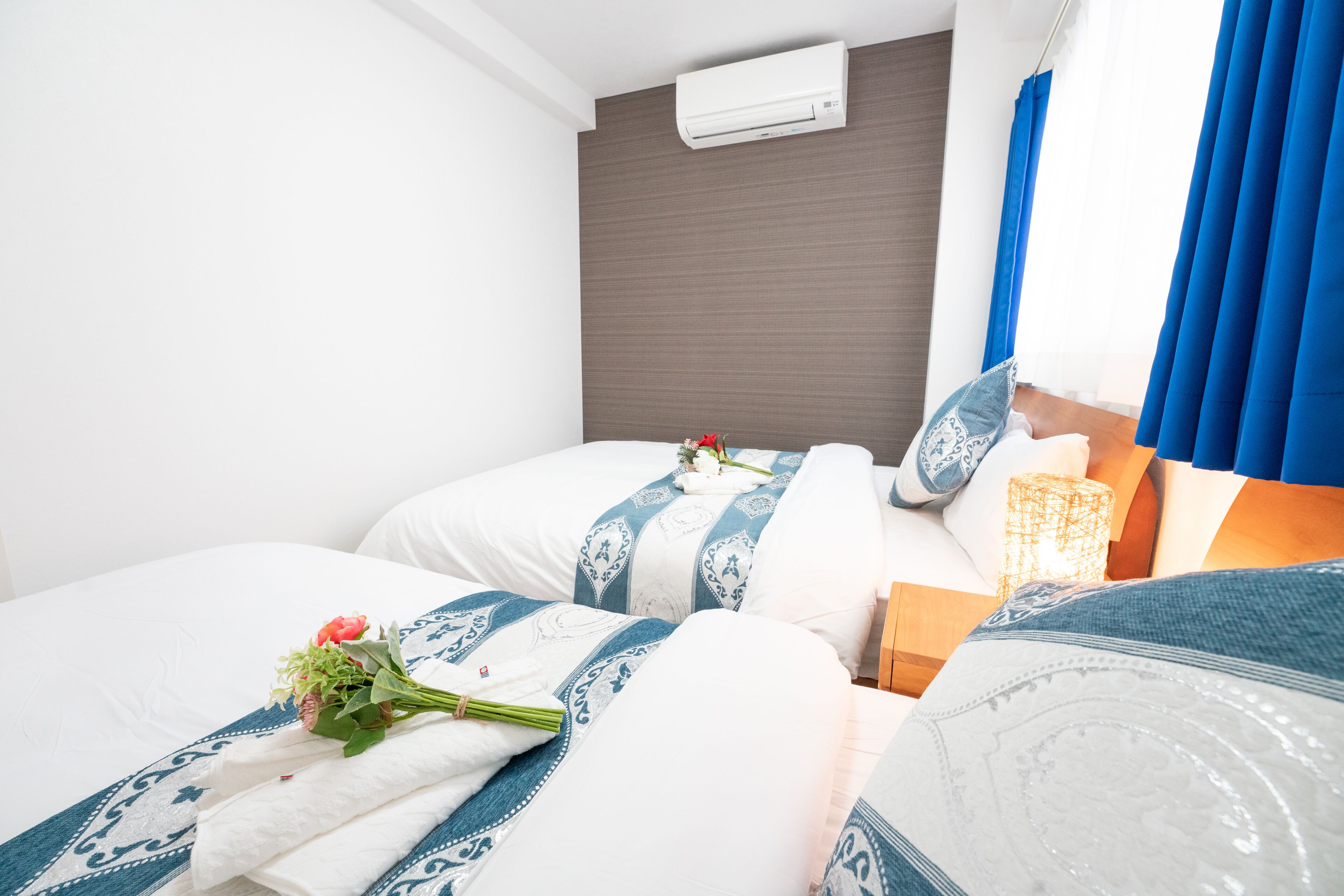 Een hotelkamer met twee bedden, een houten hoofdbord, een wandairconditioner en een nachtkastje met lamp.