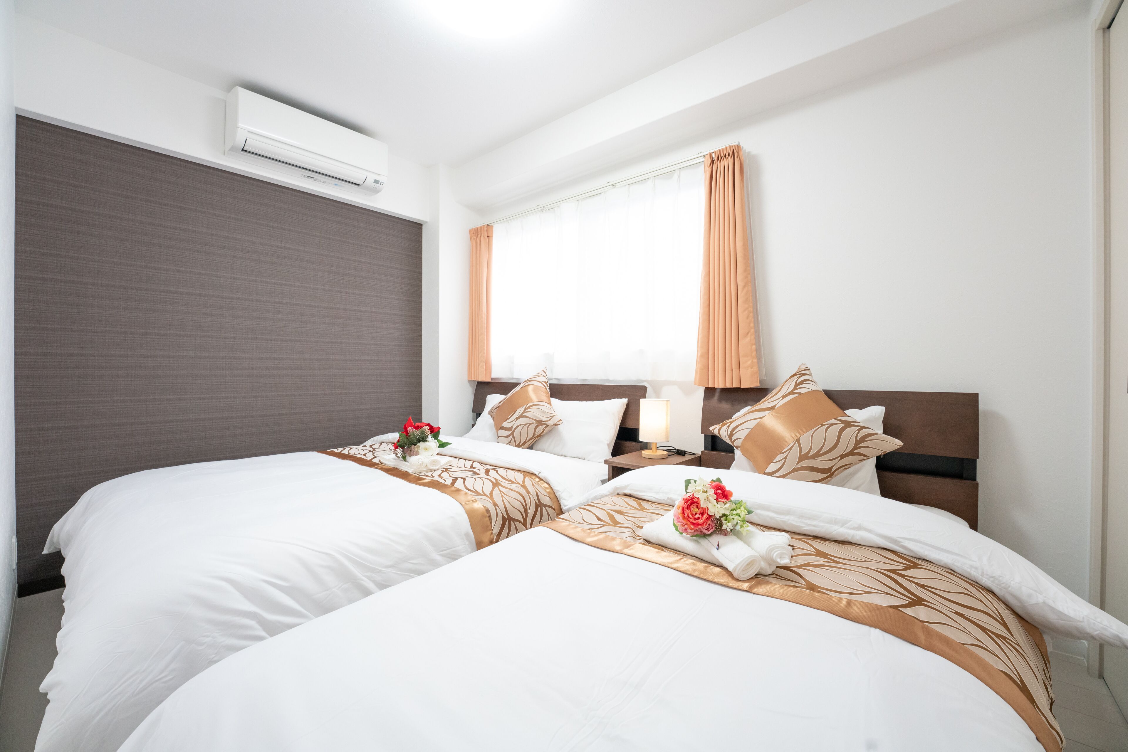 Una habitación de hotel con dos camas, un ventanal con cortinas, un aire acondicionado montado en la pared y una mesita de noche con lámpara.