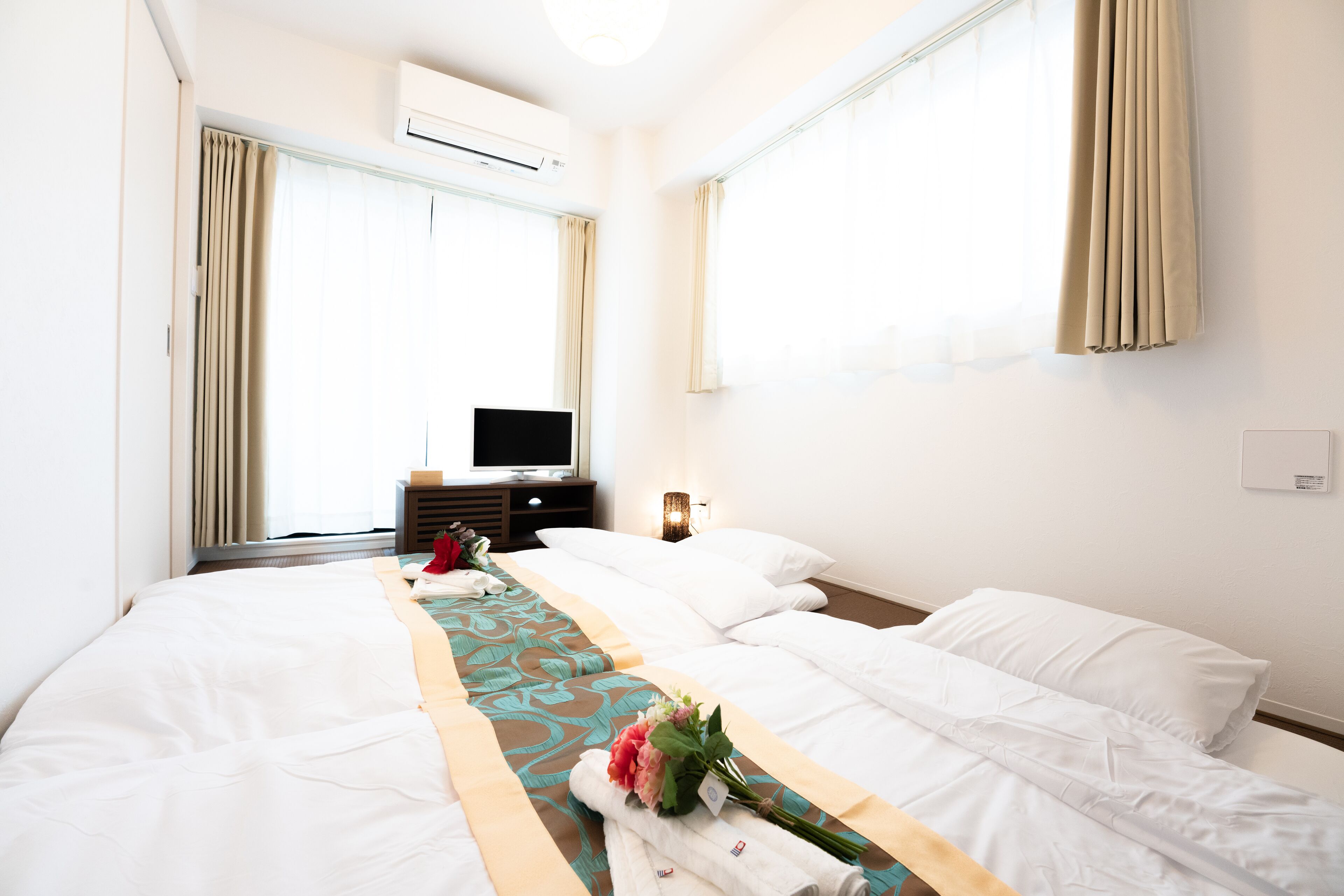 A hotel room with two beds, a TV, and an air conditioning unit.