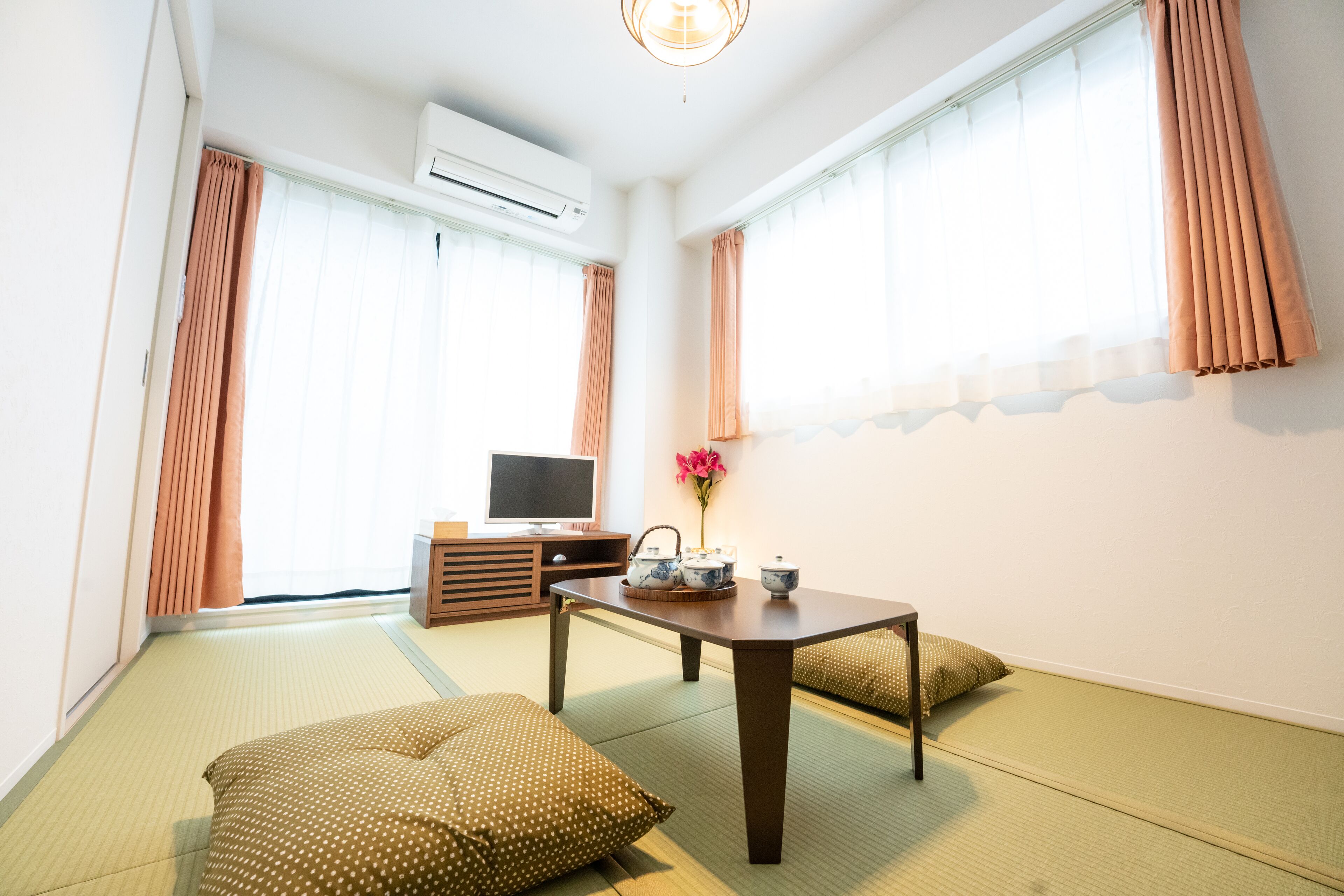 A traditional Japanese room with tatami flooring, a low table with a tea set, and a television on a wooden cabinet.
