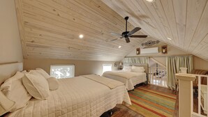 Un dormitorio acogedor en el ático con dos camas, un ventilador de techo y un colorido tapete a rayas.