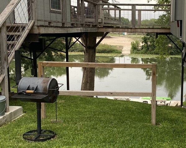En trädgård med en grill, en träbänk och utsikt över en sjö.