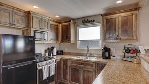 Una cocina con armarios de madera, un refrigerador, una estufa, un microondas, una cafetera y una ventana con un letrero que dice 'Welcome'.
