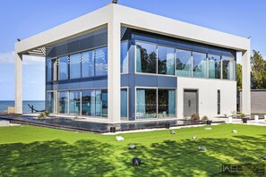 A modern two-story house with large glass windows, a swimming pool, and a well-maintained lawn.