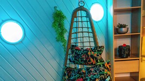 A hanging chair with a colorful floral pattern, a round window, and a shelf with a plant and a small statue. - TOWNHOUSE WITH GARDEN NEAR STATION (Dunkerque)