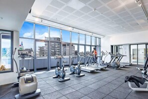 Un gimnasio moderno con diversas máquinas de cardio, amplias ventanas que ofrecen vistas a la ciudad y un diseño espacioso.