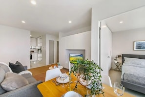A modern living room with a dining area, a grey sofa, a wooden dining table set with plates, glasses, and a plant.