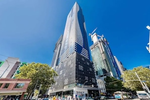 A modern high-rise building with a prominent glass facade, surrounded by other tall buildings and a busy street scene.