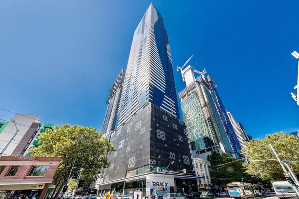 Un edificio moderno de gran altura con una fachada de vidrio destacada, rodeado de otros edificios altos y una animada calle.