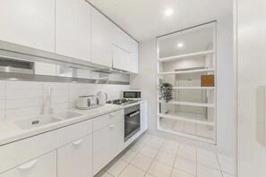 A modern kitchen with white cabinetry, a built-in oven, and a microwave. There is a small island with a sink and a plant on top.