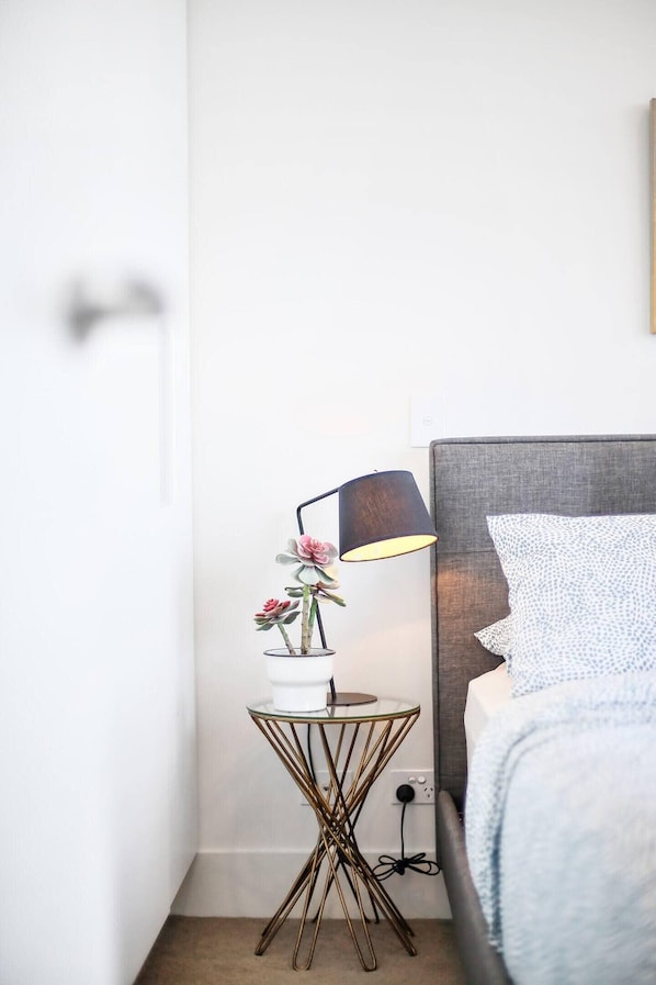 A bedroom with a bed, a bedside table with a lamp, and a wall-mounted power outlet.