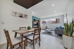 Una sala de estar moderna con comedor, un sofá gris, una mesita de centro y un amplio ventanal con vista a la ciudad.