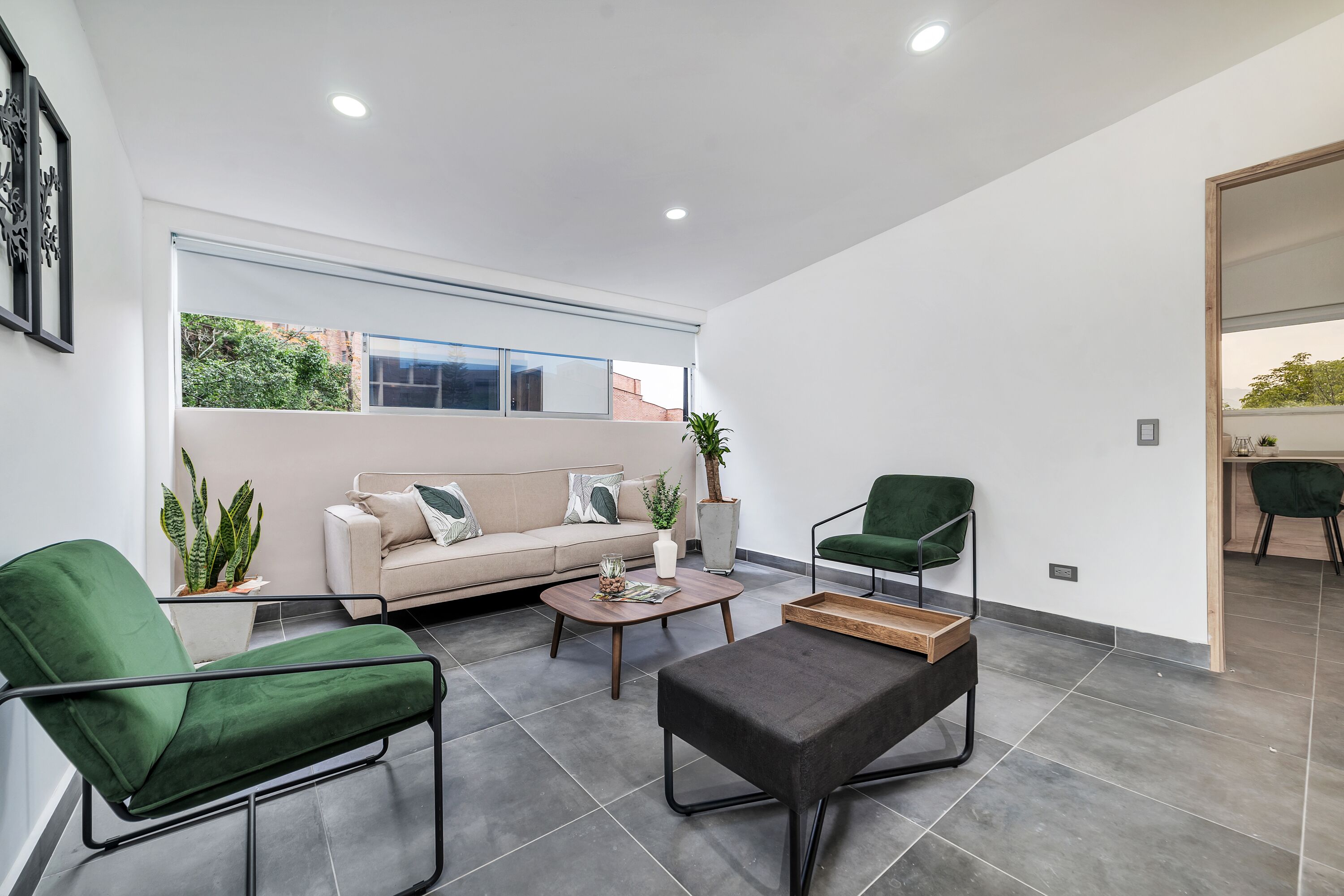 A modern living room with a sofa, two green armchairs, a coffee table, and a small wooden table.