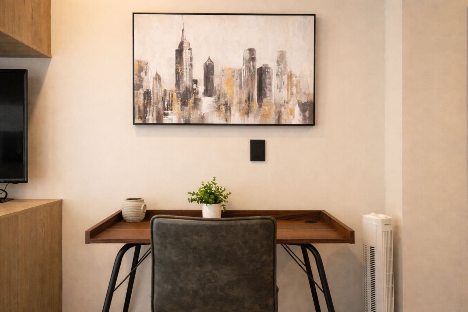 Una habitación con una pintura de paisaje urbano, un escritorio con una planta en maceta, una silla y un radiador.