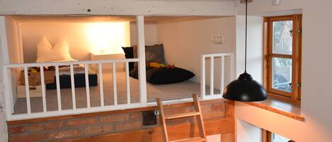 Dormitorio tipo loft con escalera de madera, cuna blanca y ventana con vistas.