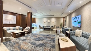 Un salón amplio con un tapete grande, diversas opciones de asientos que incluyen sofás y sillones, una mesa de centro y un televisor montado en la pared.