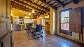 A rustic kitchen with wooden beams, a dining area with a table and chairs, and a large window with a view of potted plants. - CAN FELIP Penthouse with Fantastic Views (Palafrugell)