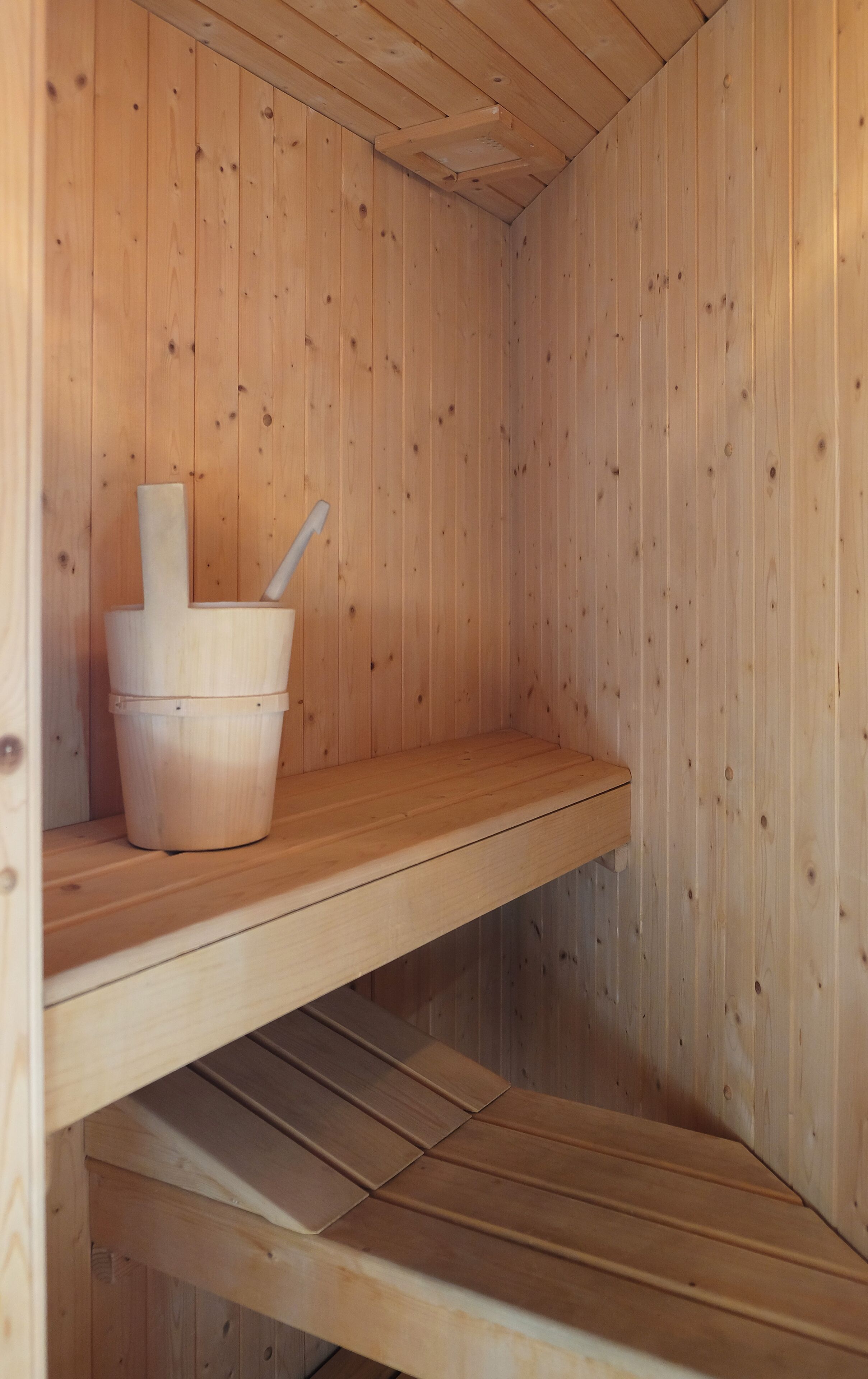 A wooden sauna with a wooden bench and a bucket with a ladle.