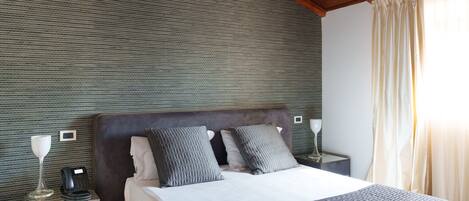 A hotel room with a large bed, a bedside table with a lamp, a telephone, and a wall-mounted control panel.