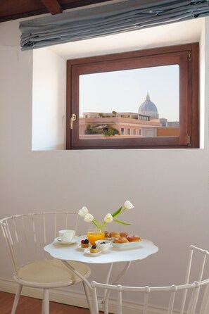 A small dining area with a table set for breakfast, a window with a view of a building, and a chair. - The Place 217 (Rome)