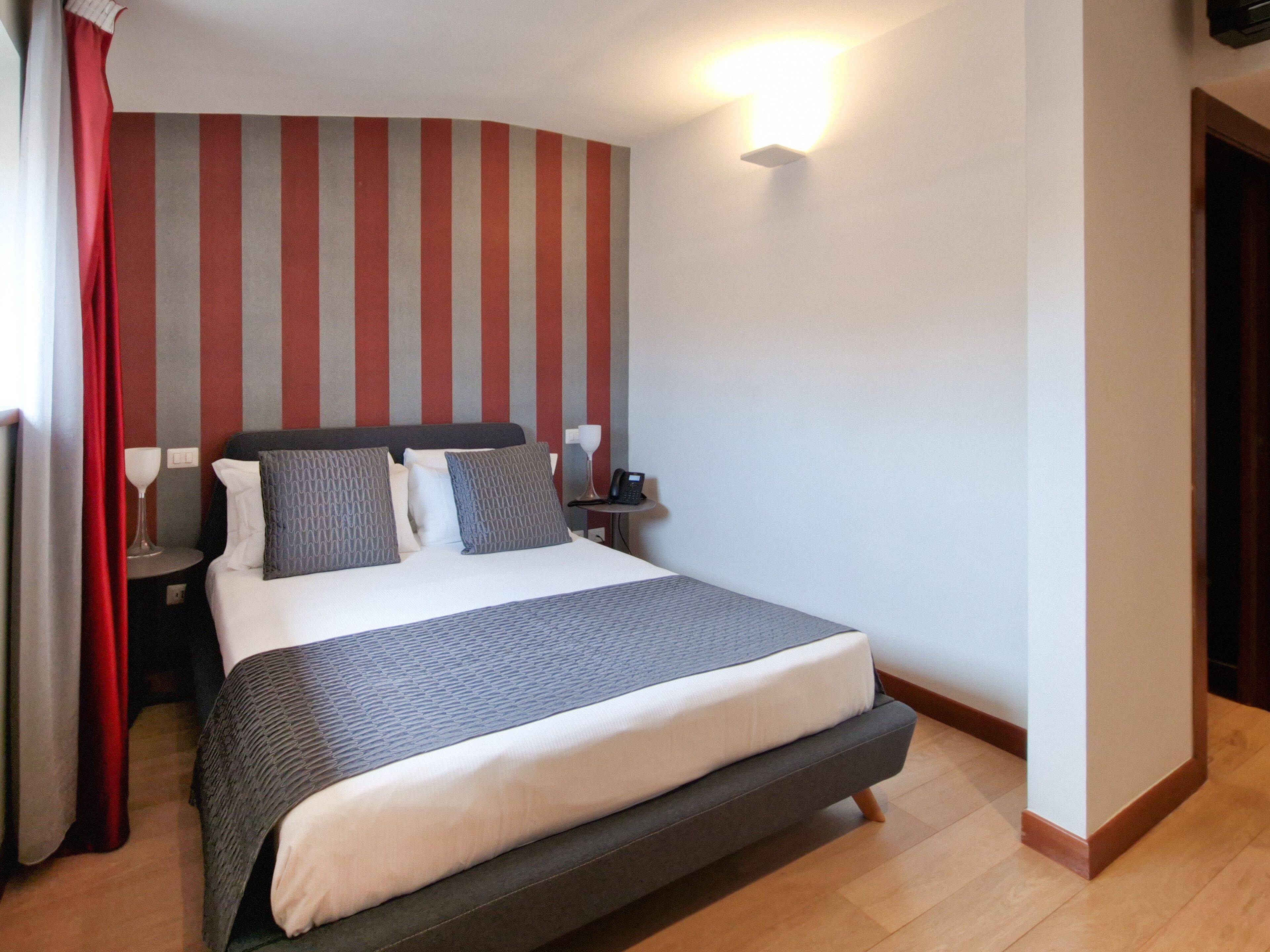 Habitació d'hotel moderna amb un llit gran, una taula de nit amb una làmpada i una paret amb dibuixos de ratlles.