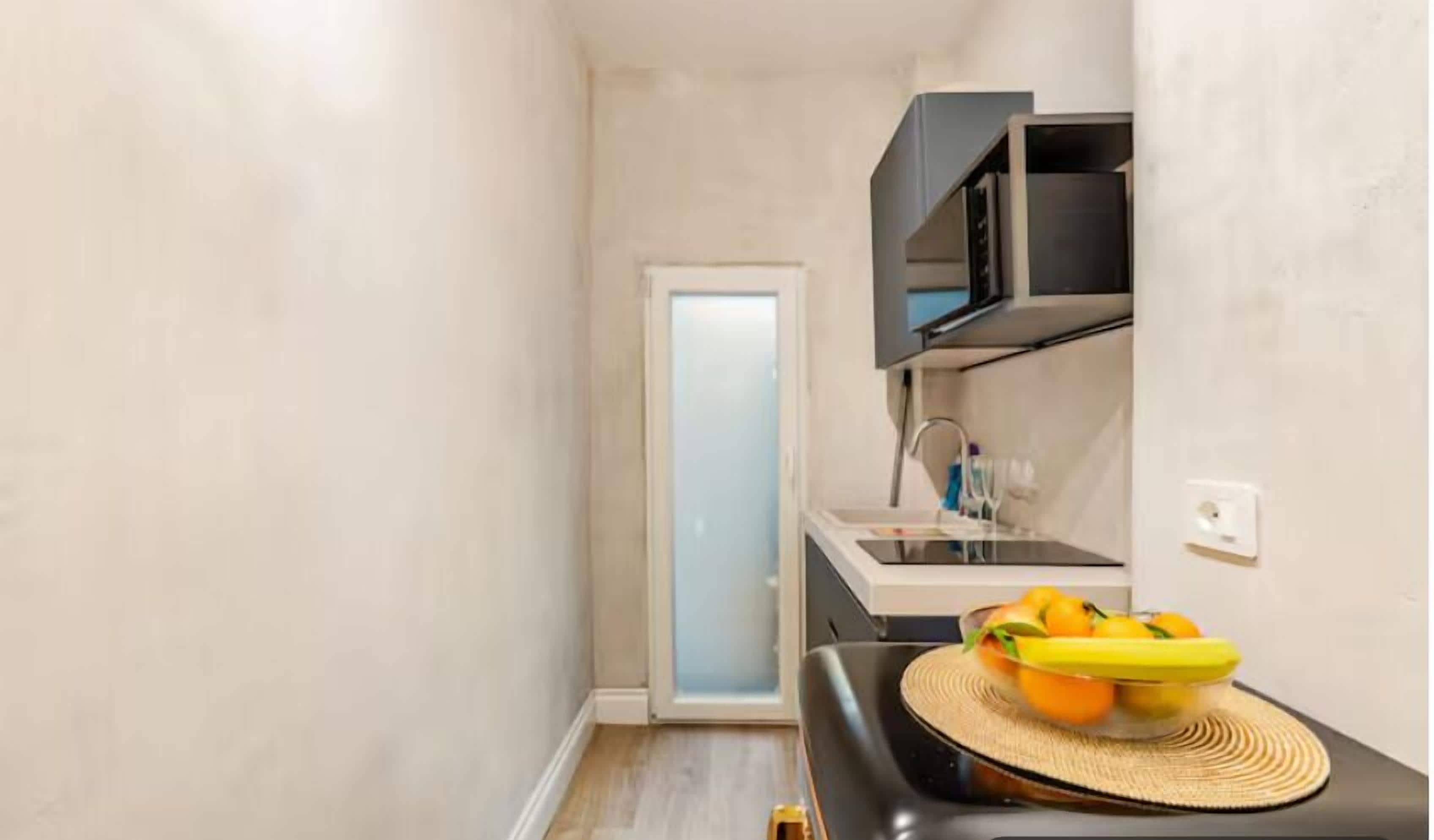 A narrow kitchen with a microwave, sink, and a bowl of fruit on the counter.