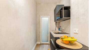 A narrow kitchen with a microwave, sink, and a bowl of fruit on the counter.