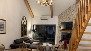 A cozy living room with a fireplace, wooden staircase, and a dining area with a round table and chairs.
