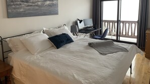 A hotel room with a large bed, a desk with a computer, a chair, and a balcony with a railing.
