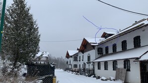 A snow-covered street with traditional buildings, a fence with a red and white sign, and a utility pole.