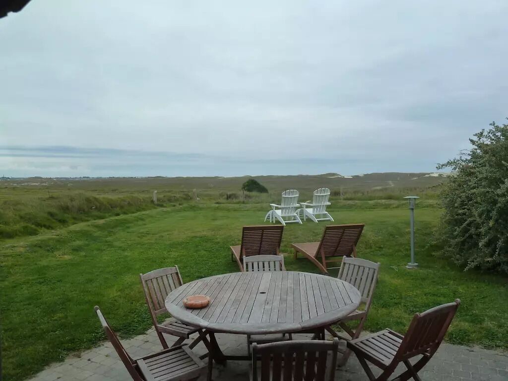 A round wooden table with six chairs in a grassy outdoor area, with a view of the landscape in the background.