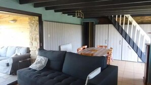 A living room with a dark sofa, a dining table with chairs, and a staircase. - Kerdu Pointe de la Torche - 200 m from the beach (Plomeur)