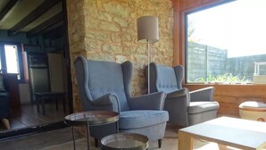 A modern living room with a stone wall, a large window, a grey sofa, a round coffee table, and a wooden table. - Kerdu Pointe de la Torche - 200 m from the beach (Plomeur)