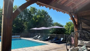 Eine Holzterrasse mit Pool, Liegestühlen und Sonnenschirmen.