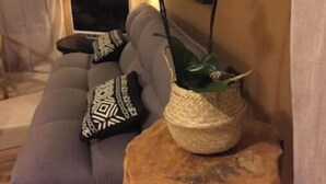 Ein Wohnzimmer mit grauem Sofa, einem gewebten Blumentopf und einem hölzernen Hocker.