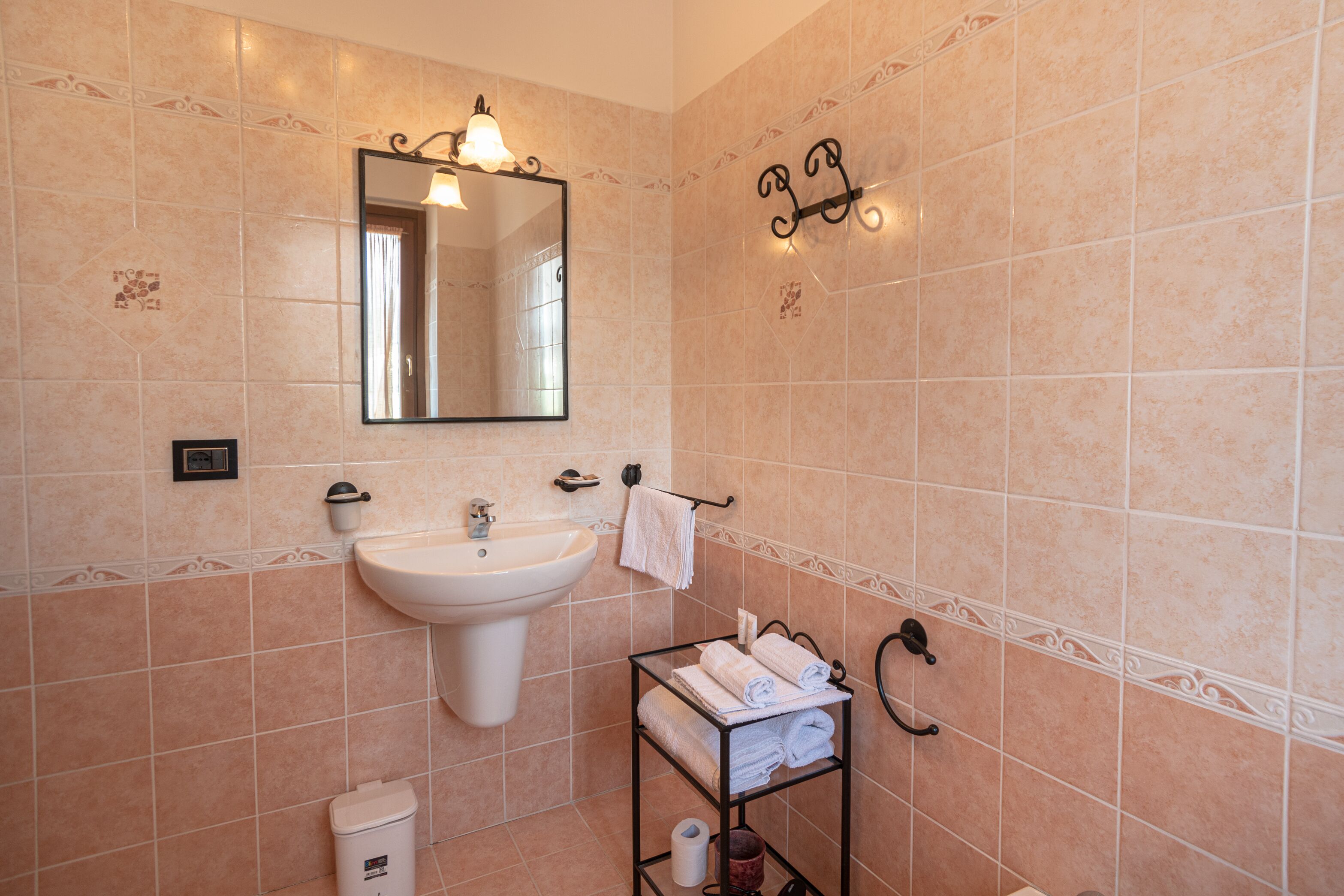 A bathroom with beige tiles, a white sink, a mirror, and a towel rack with towels.