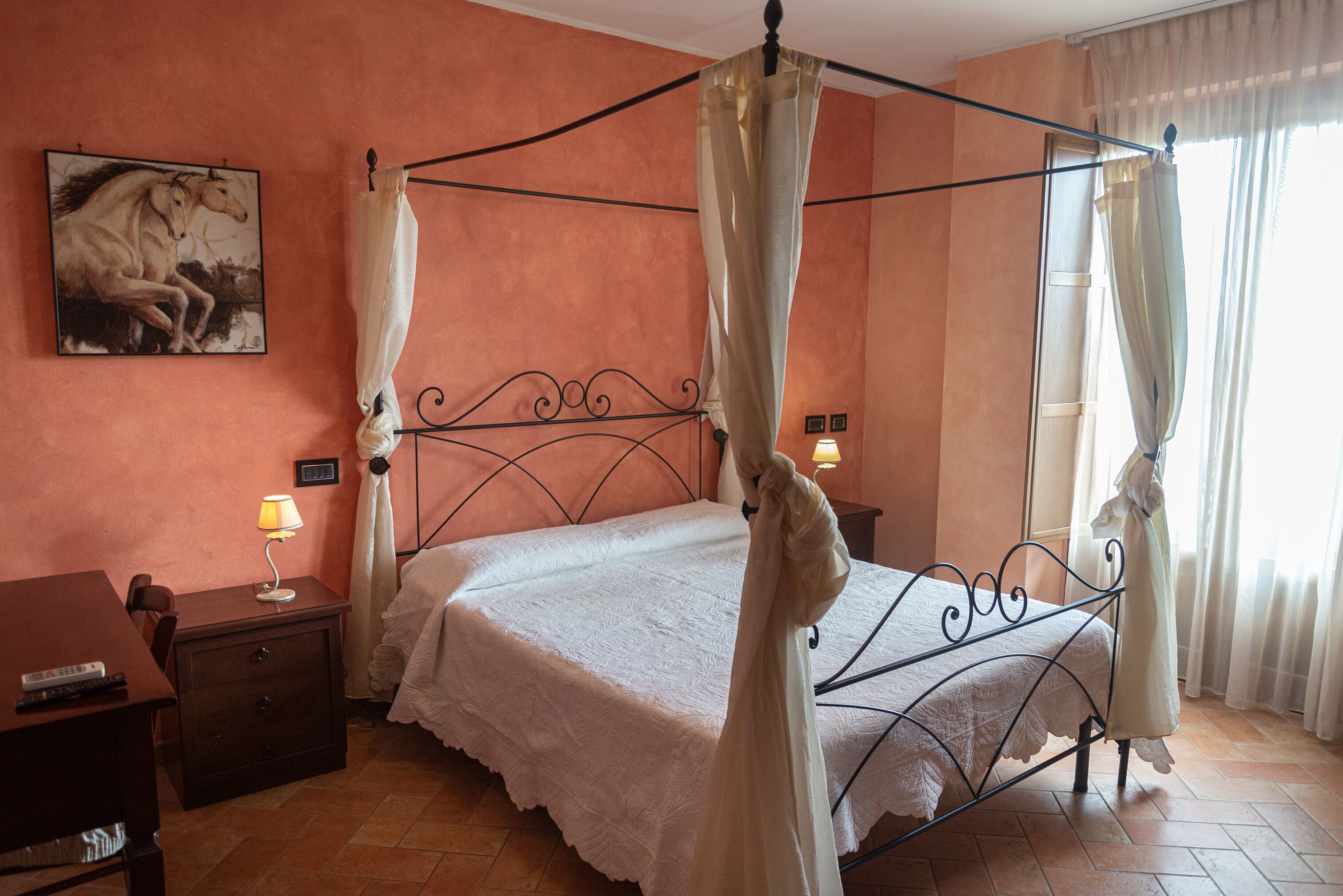 A four-poster bed with a white bedspread, a nightstand with a lamp, and a painting of horses on the wall.