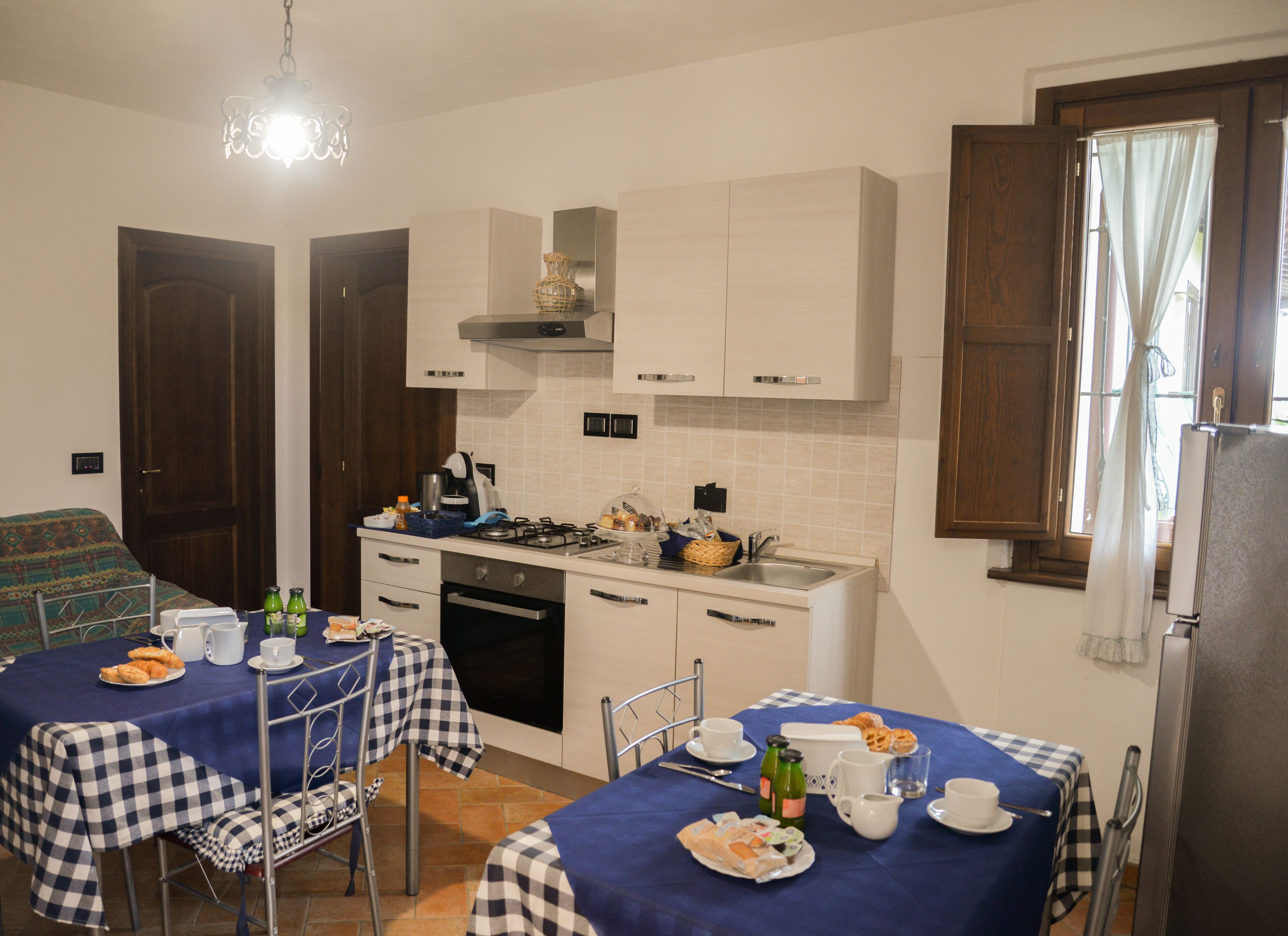 Una cucina compatta con mobili bianchi, piano cottura a gas e zona pranzo con tovagliette a scacchi.